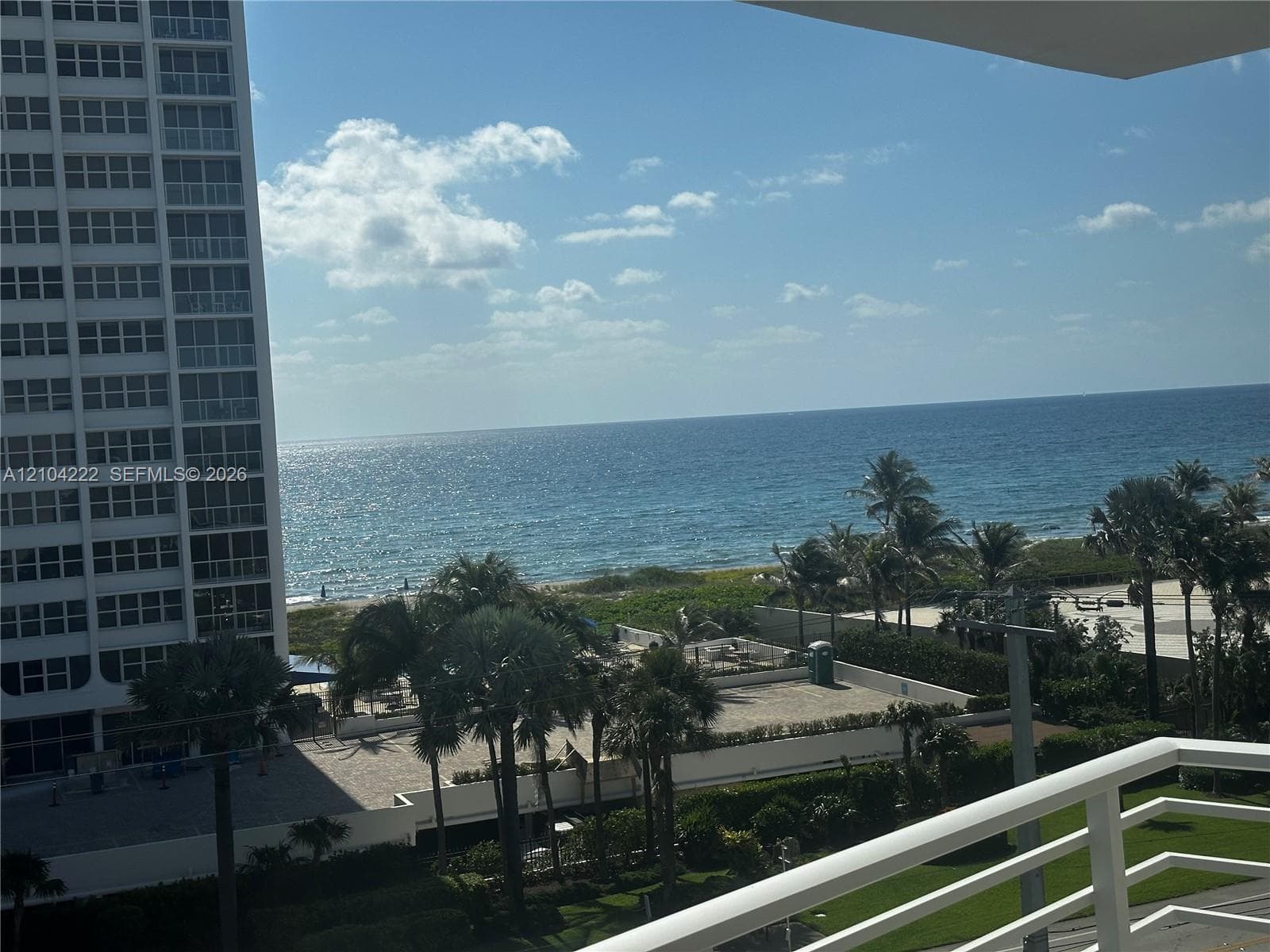 Balcony featuring a white railing, ocean scenery, and mature palm trees