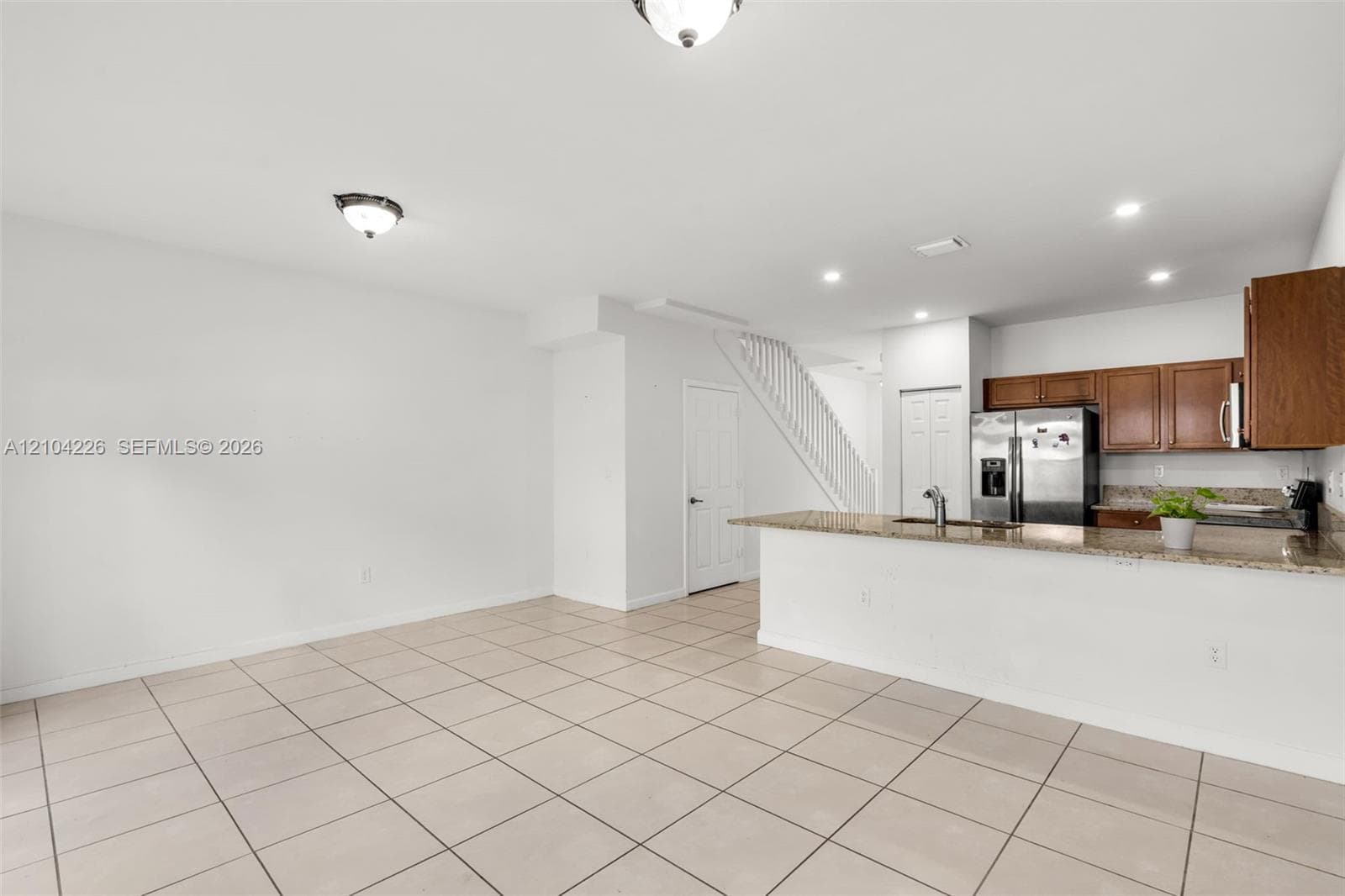 Kitchen featuring stone-finish countertops, stainless steel appliances, and wood-finish cabinetry, complemented by tile flooring and recessed lighting