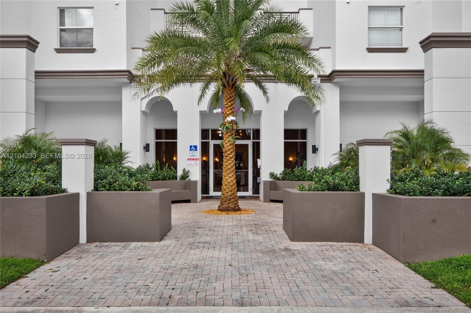 Exterior entryway featuring arched architectural detailing, paver stone walkway, and built-in masonry planters