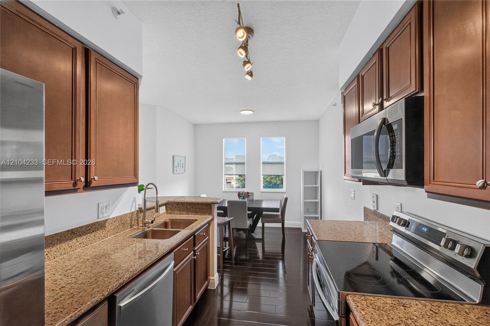 Kitchen featuring wood cabinetry, stone countertops, double-basin sink, stainless steel appliances, and wood-finish flooring