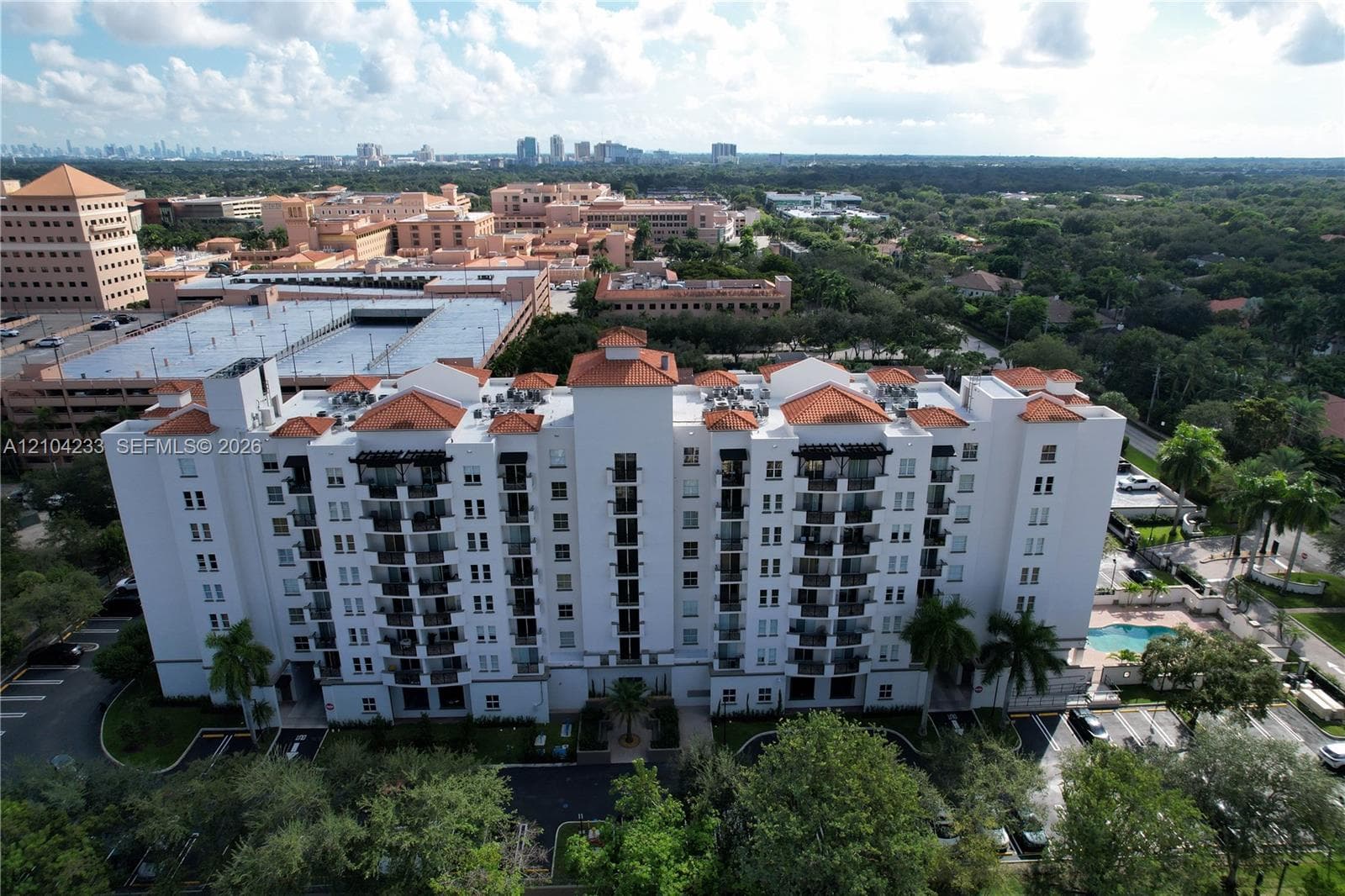 Multi-story building with a light-colored facade, terracotta-tiled roof, recessed private balconies, and an outdoor swimming pool