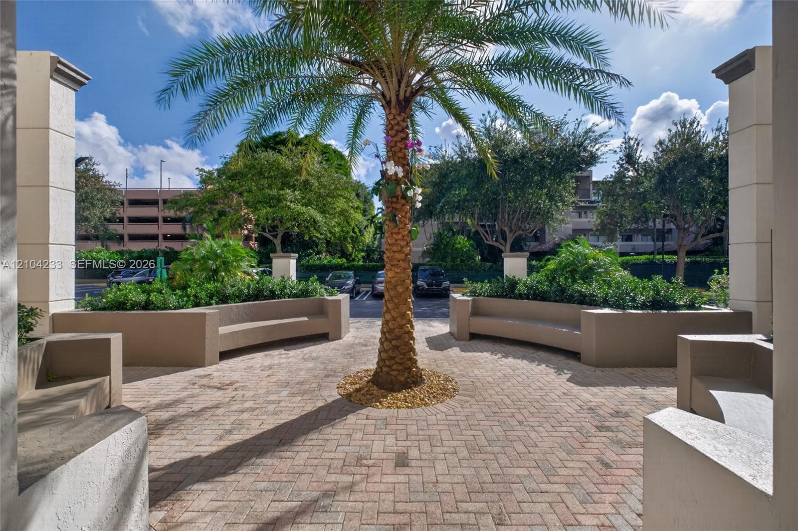 Courtyard area featuring herringbone-patterned paver flooring, built-in masonry benches, and central landscaping with a palm tree