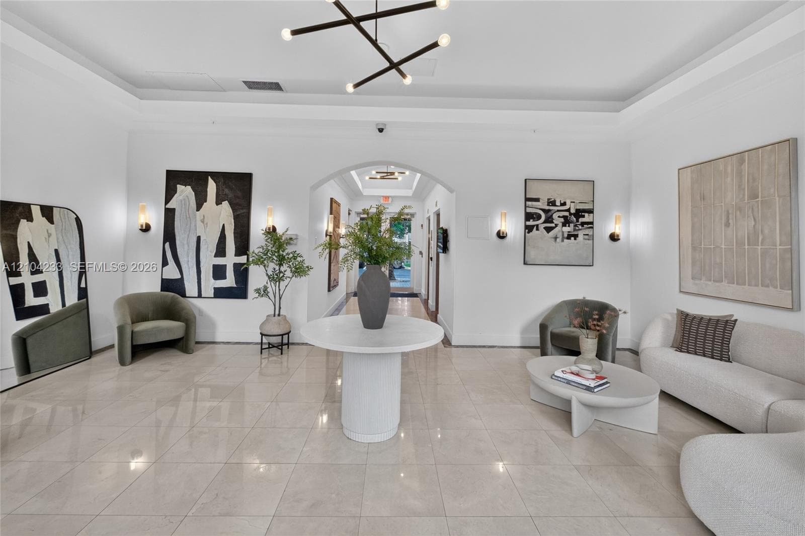 Polished tile flooring, tray ceilings, recessed arched entry, contemporary geometric chandelier, and wall-mounted sconces