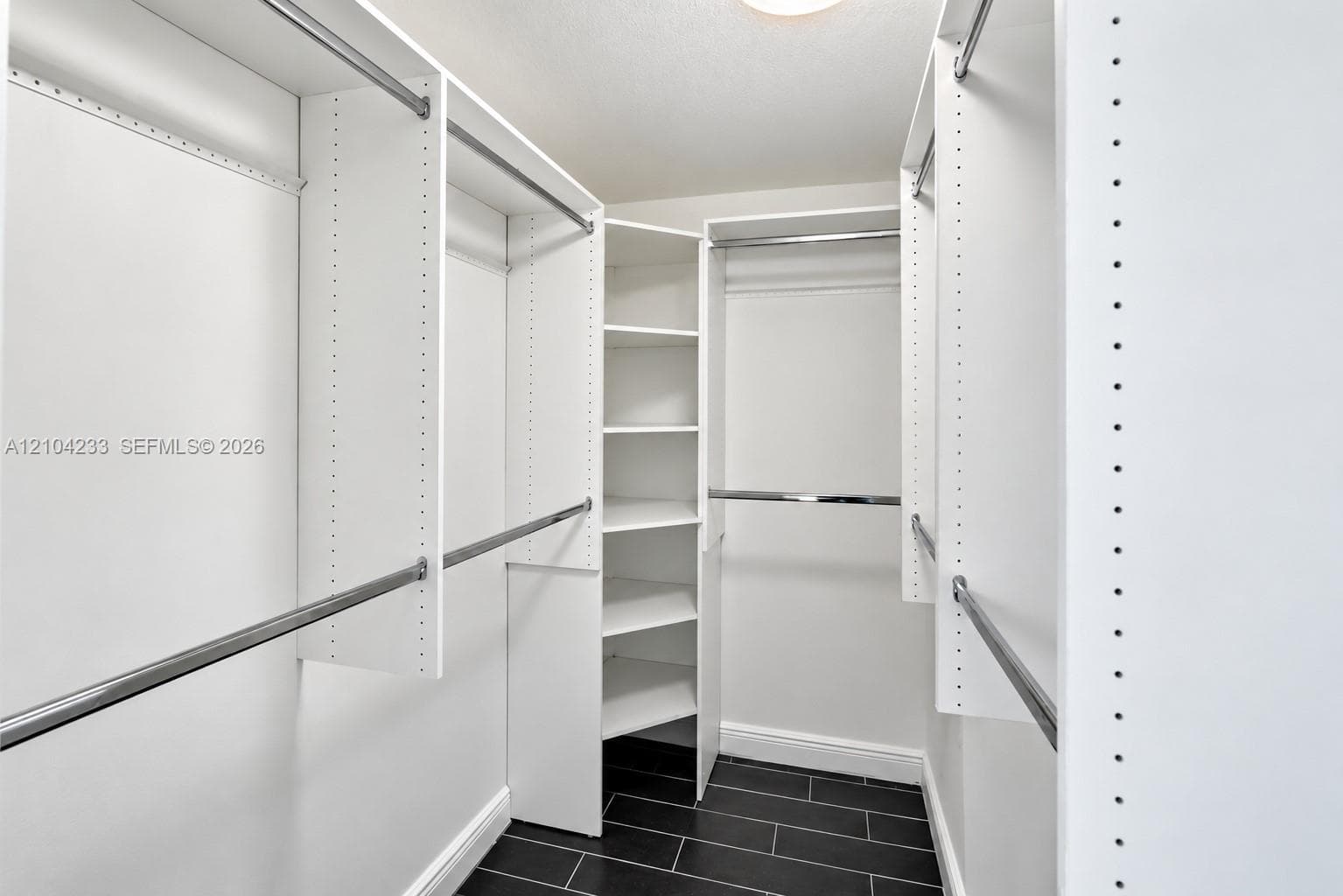 Walk-in closet featuring white built-in shelving, adjustable storage cubbies, metal hanging rods, and dark tile flooring