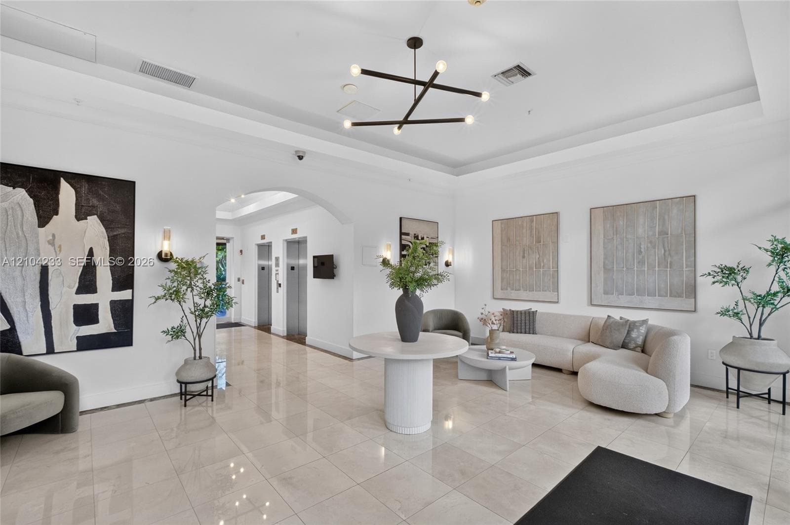 Lobby featuring high tray ceilings, polished tile flooring, metallic elevator doors, and a multi-arm modern pendant light fixture