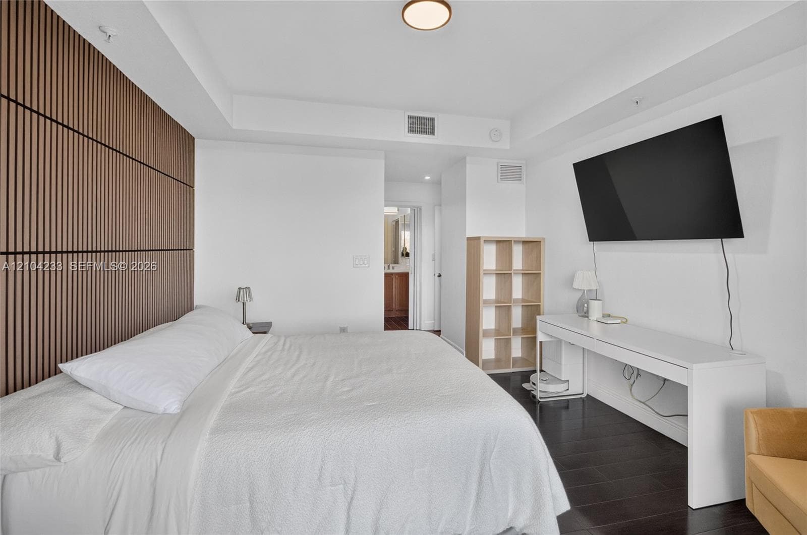 Bedroom featuring dark wood-finish flooring, a floor-to-ceiling slatted wood accent wall, recessed lighting, and a tray ceiling