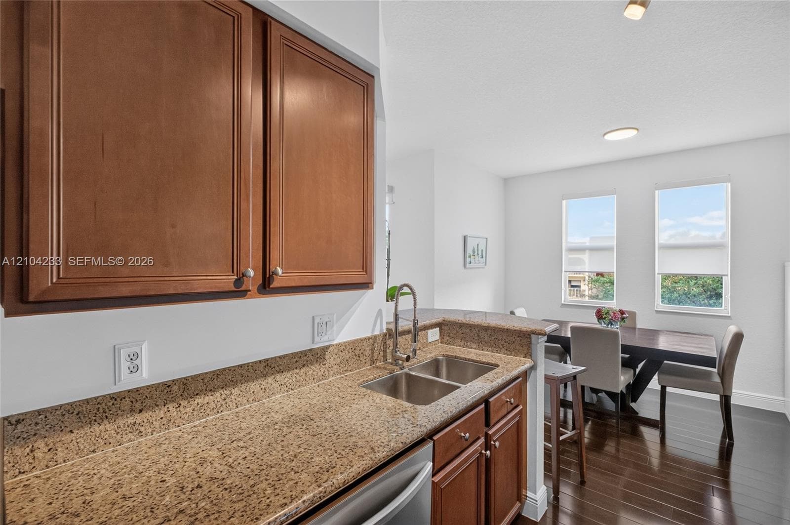 Kitchen featuring wood cabinetry, stone-surface countertops, dual-basin stainless steel sink with high-arc faucet, and wood-finish flooring