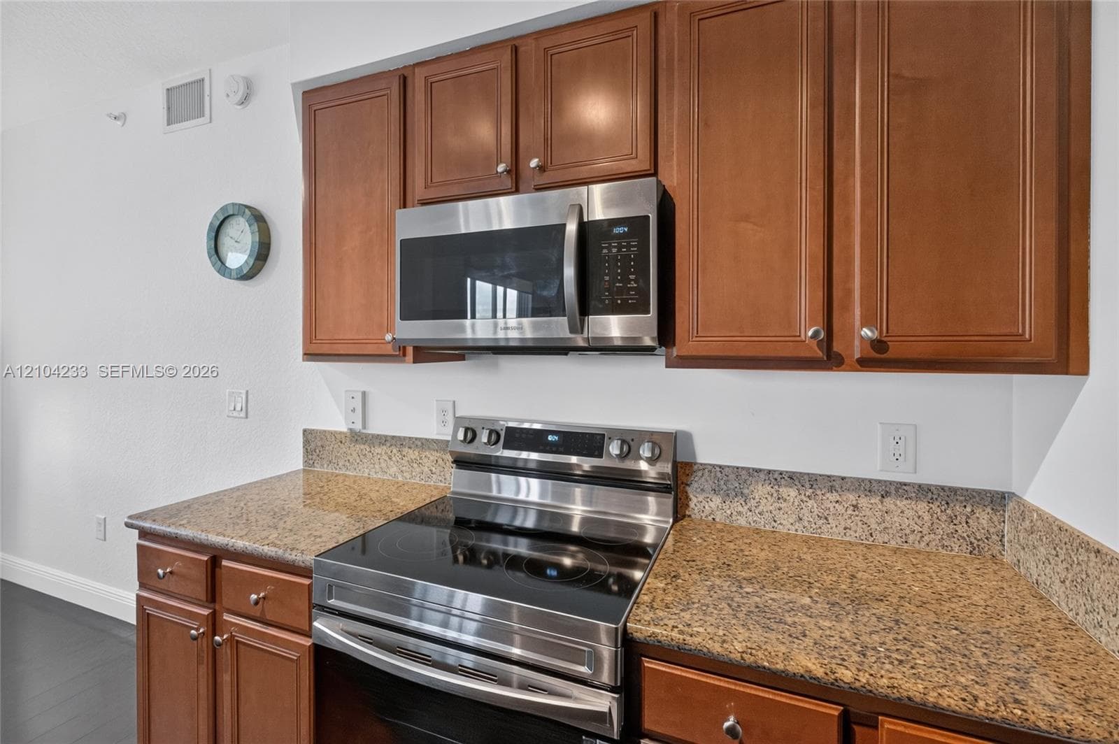 Kitchen featuring stained wood cabinetry, stone-surface countertops, and stainless steel appliances including a built-in microwave and range