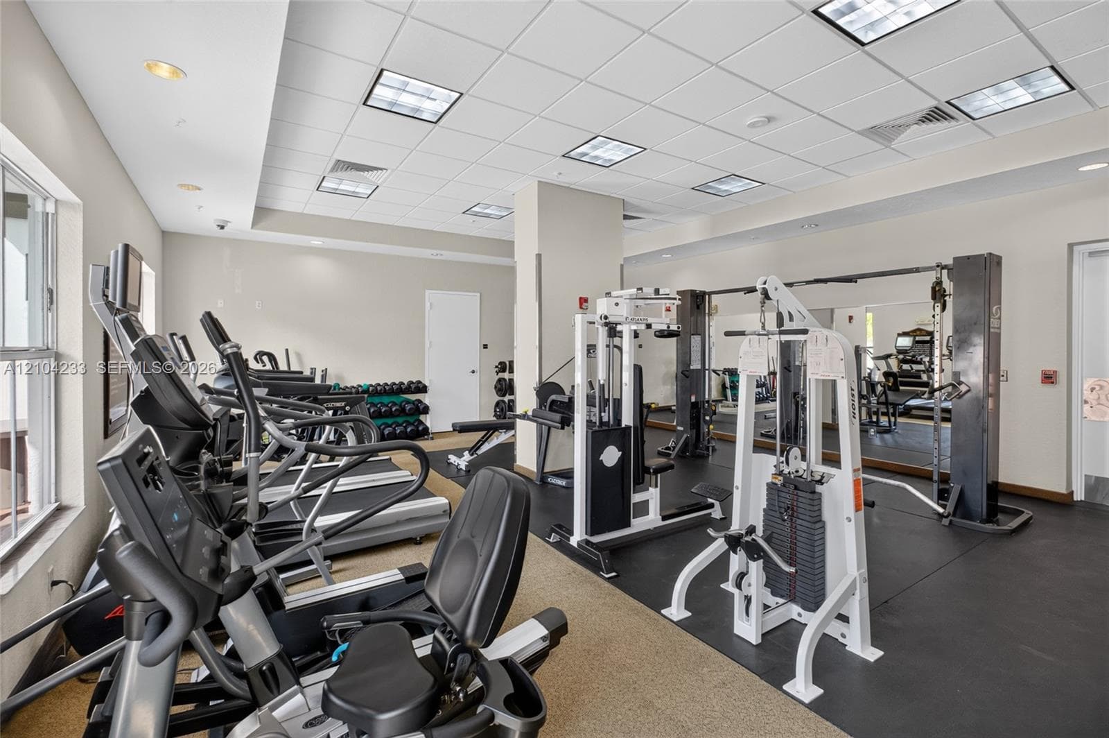 Fitness center featuring drop ceiling tiles, recessed lighting, wall-to-wall rubber flooring, and large mirrored walls