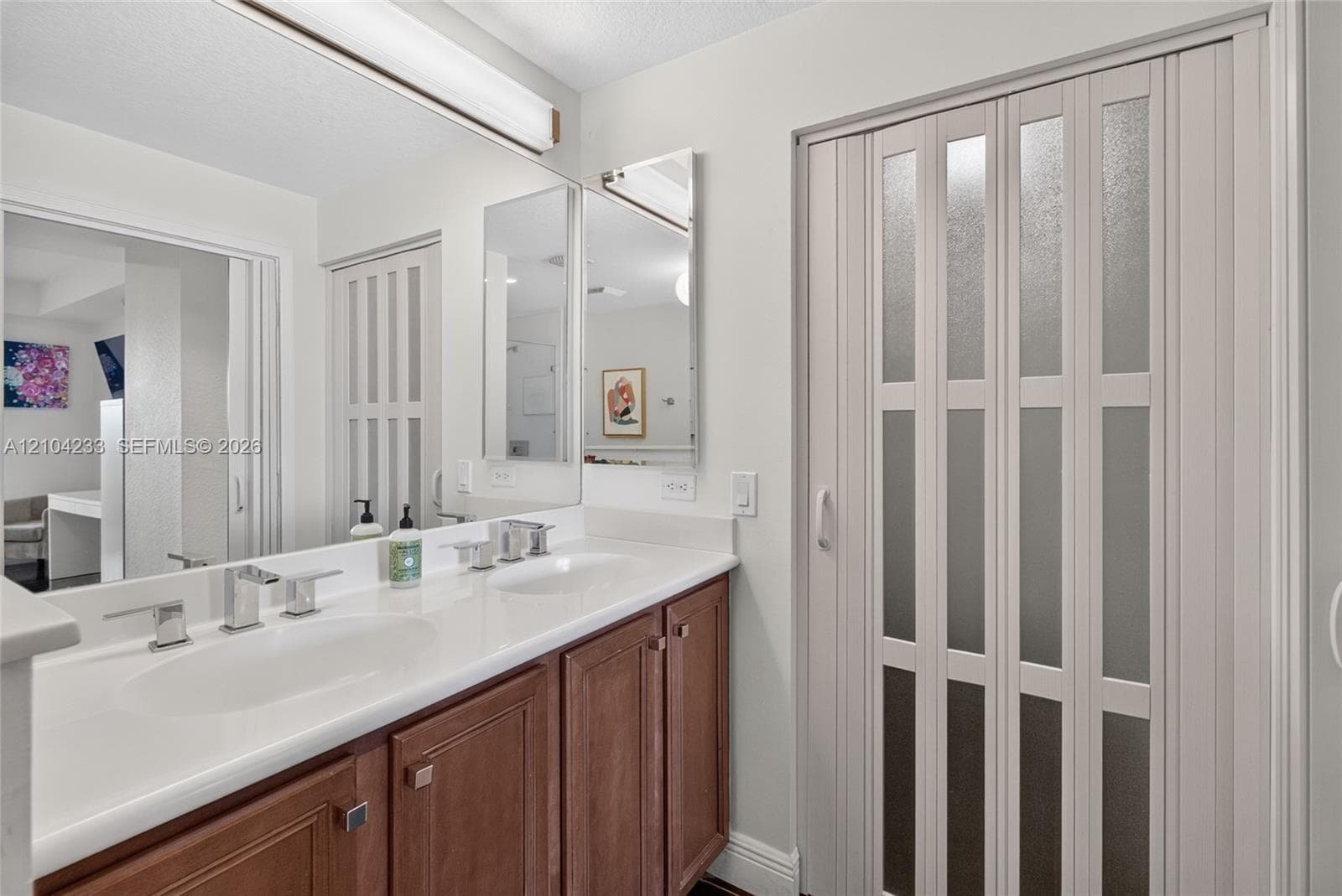 Dual-sink vanity with white countertop, integrated sinks, chrome fixtures, full-width mirror, and bi-fold door with frosted glass panels