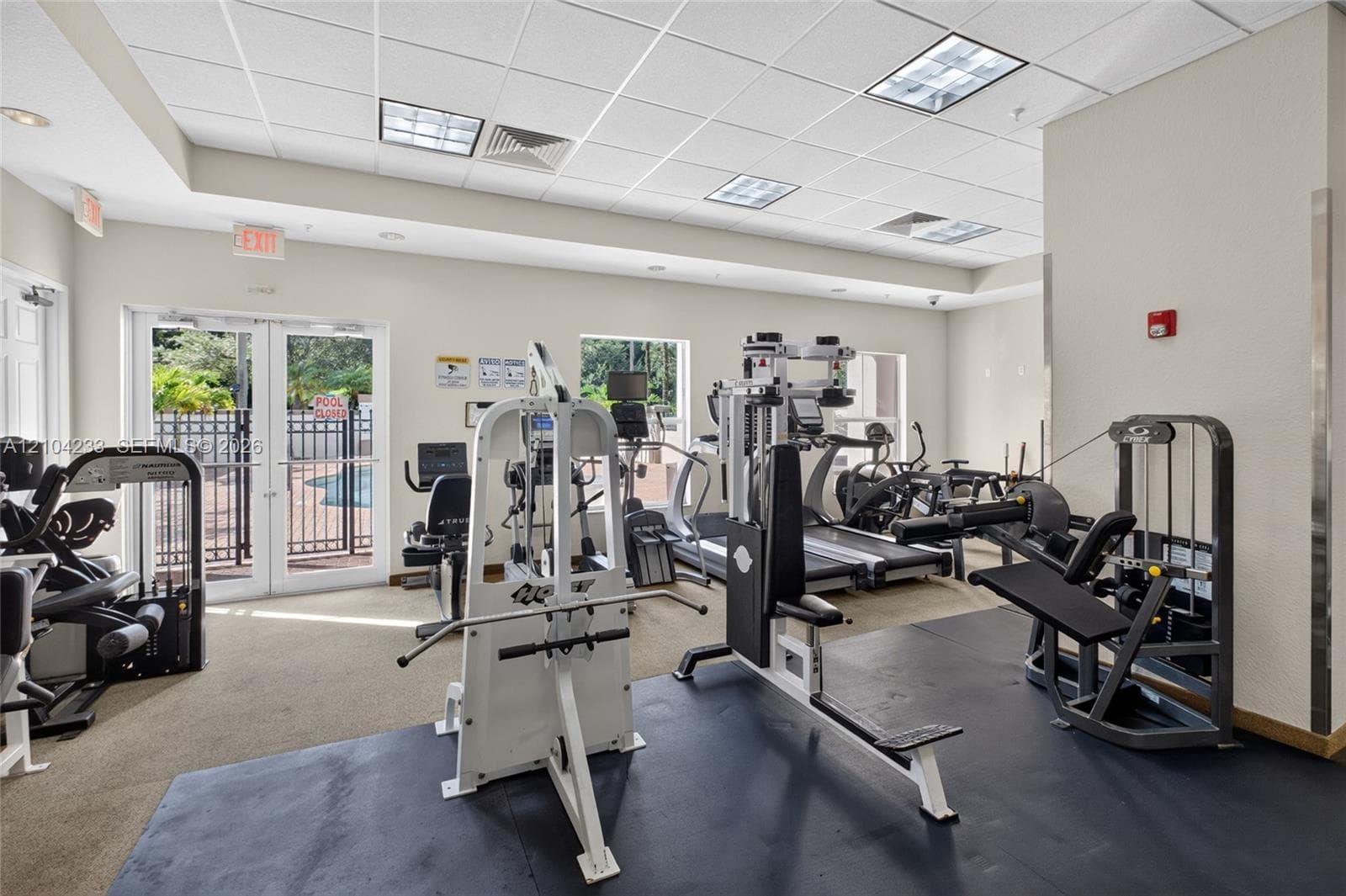 Fitness center featuring a drop ceiling with recessed panel lighting, neutral wall paint, and double glass doors providing exterior exposure