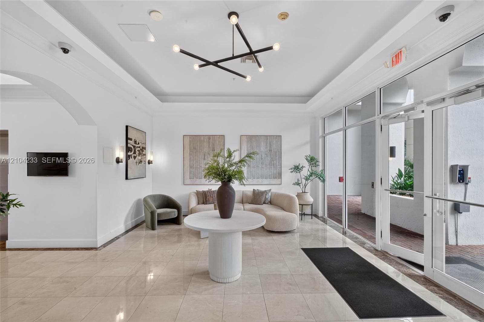 Reception lobby featuring polished stone flooring, tray ceilings, contemporary geometric chandelier, and floor-to-ceiling glass wall panels