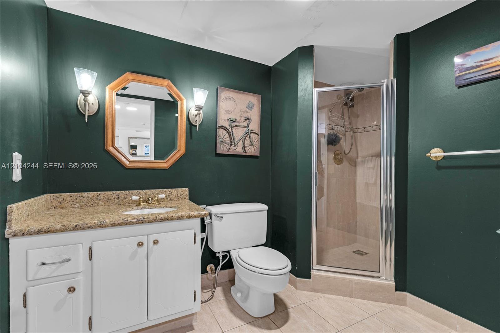 Bathroom featuring a white vanity cabinet with stone-finish countertop, undermount sink, dual wall-mounted light fixtures, and a glass-enclosed shower stall with tiled surround