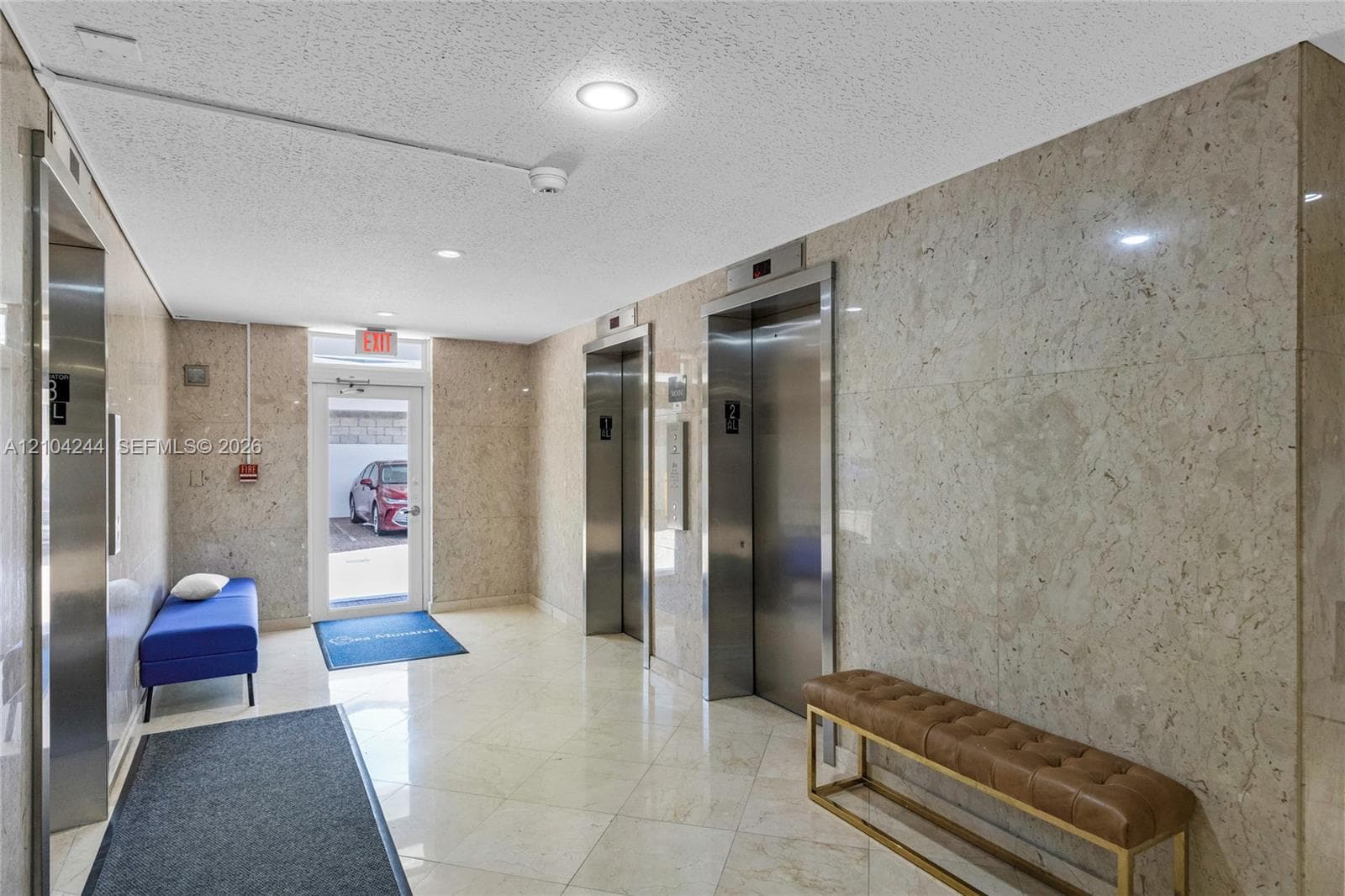 Lobby area featuring full-height natural stone wall cladding, polished stone flooring, and dual stainless steel elevator doors
