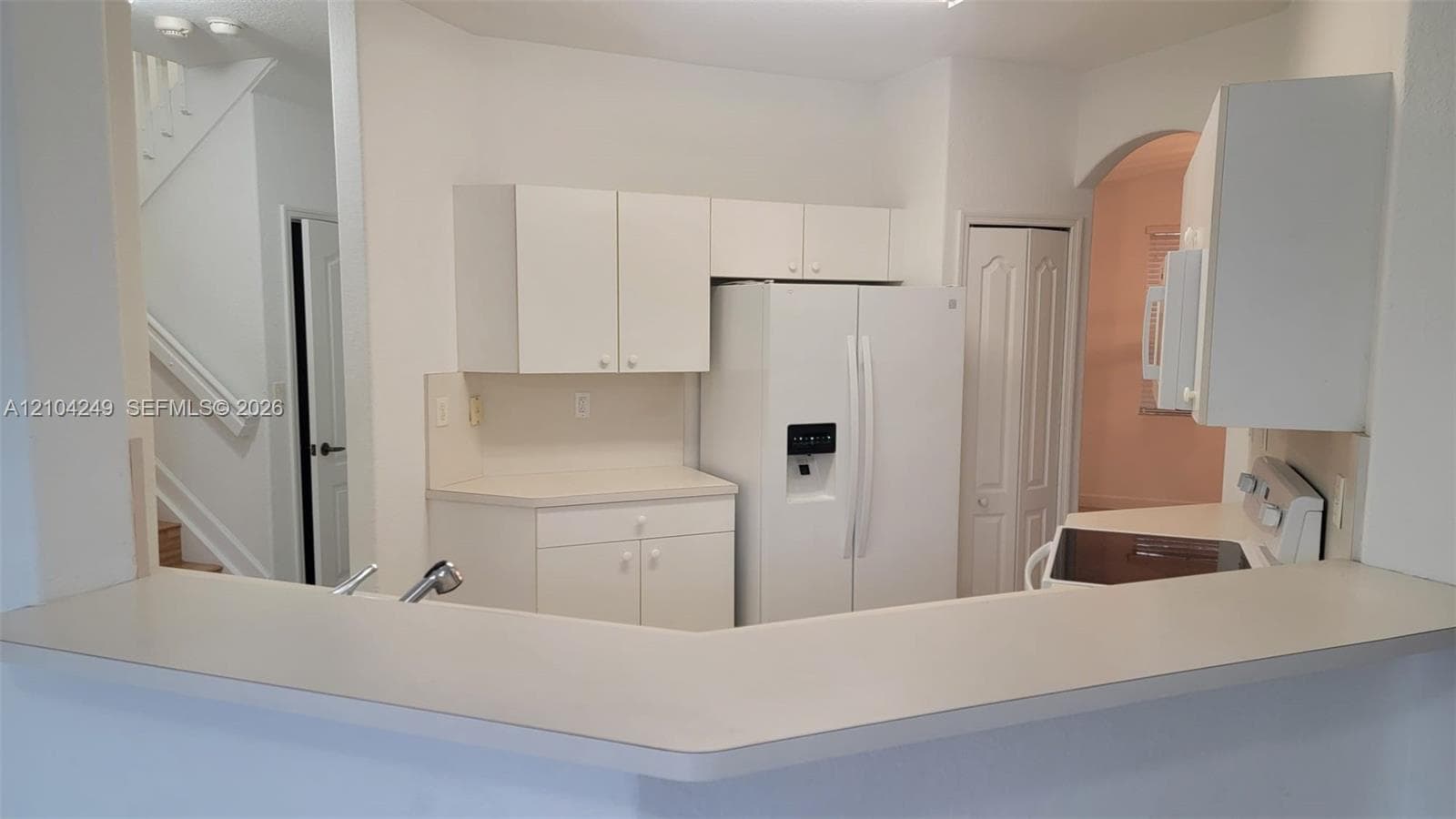 Kitchen featuring white cabinetry, a neutral-toned countertop, a pass-through breakfast bar, and integrated white appliances
