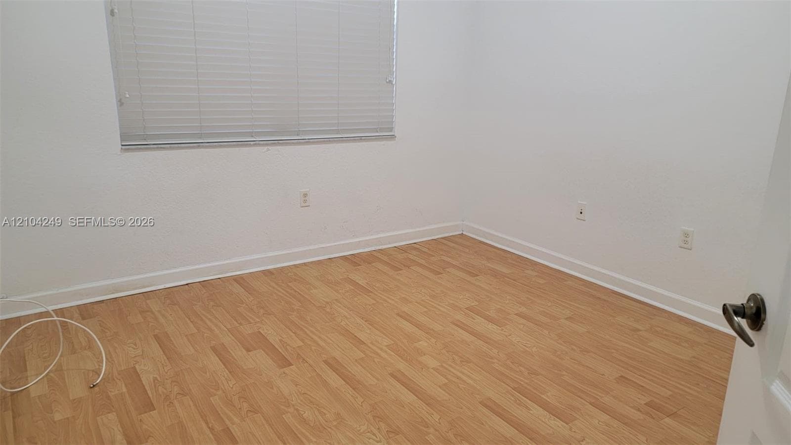 Downstairs bedroom featuring wood-finish flooring, white walls, and a window with horizontal blinds