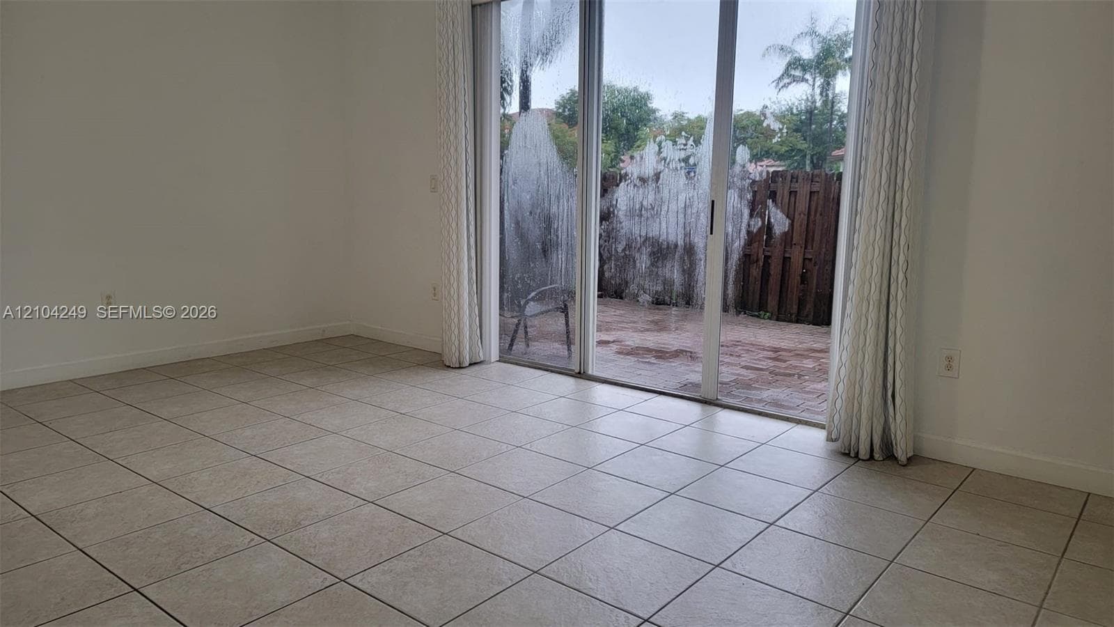 Neutral-toned ceramic tile flooring, sliding glass door, and enclosed outdoor patio with wood fencing