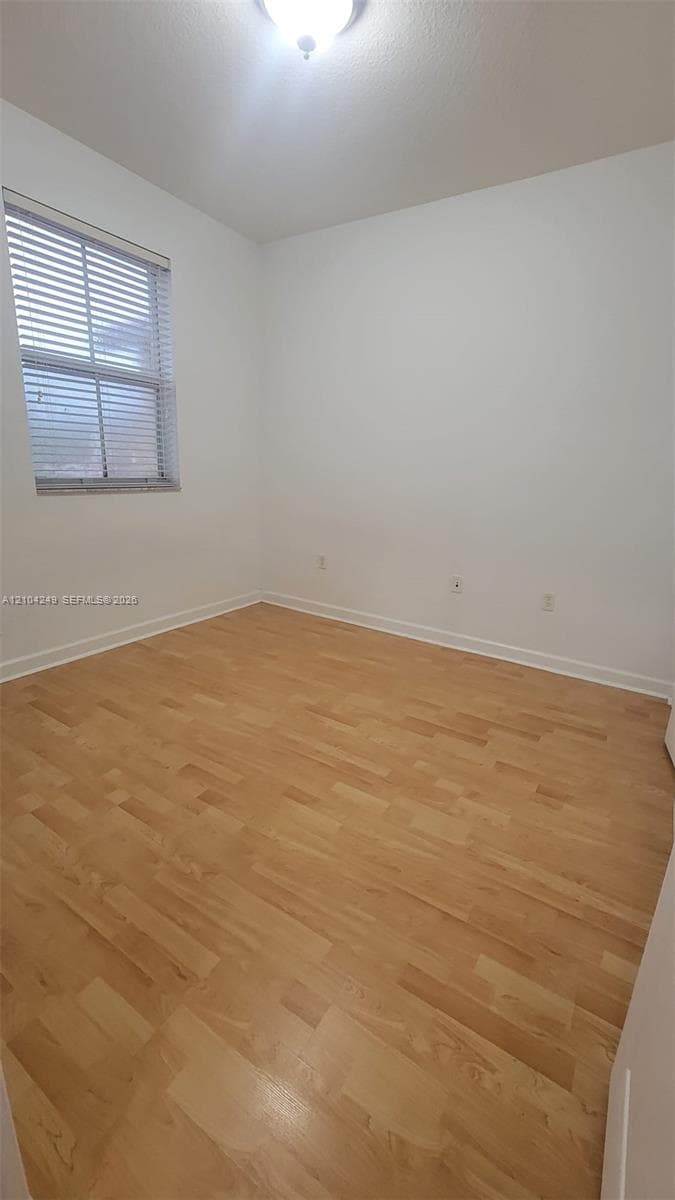 Wood-finish flooring, neutral walls, single-pane window with horizontal blinds, and a dome-style flush-mount ceiling light