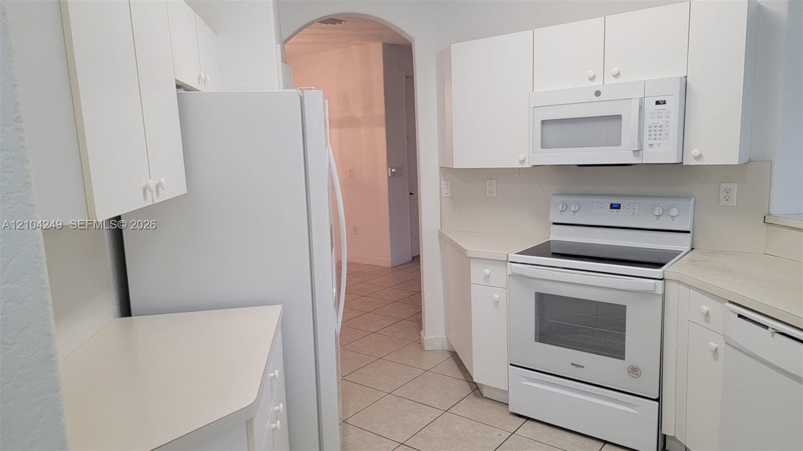 Kitchen featuring white cabinetry, light-toned countertops, tile flooring, and white built-in appliances including a range, microwave, and refrigerator