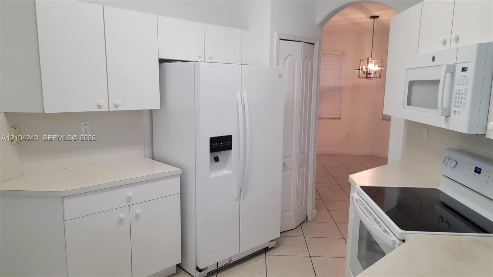 Kitchen featuring white cabinetry, light-toned solid surface countertops, tile flooring, and integrated white appliances including a side-by-side refrigerator, electric range, and over-the-range microwave