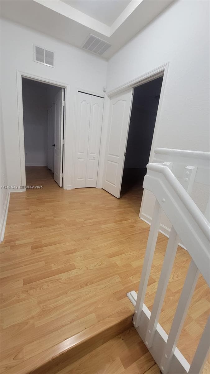 Hallway featuring wood-finish flooring, white paneled interior doors, and a recessed ceiling detail with a white staircase railing