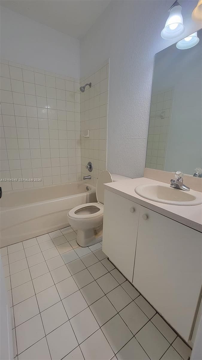 Downstairs bathroom featuring a tub-shower combination with ceramic tile surround, white vanity cabinet with a neutral countertop, recessed sink basin, and ceramic floor tiling