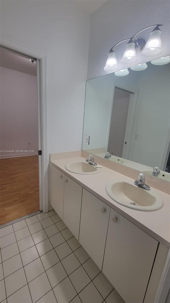 2nd bathroom upstairs  Double vanity featuring integrated oval sinks, a full-width wall mirror, wood-finish cabinetry, and ceramic tile flooring