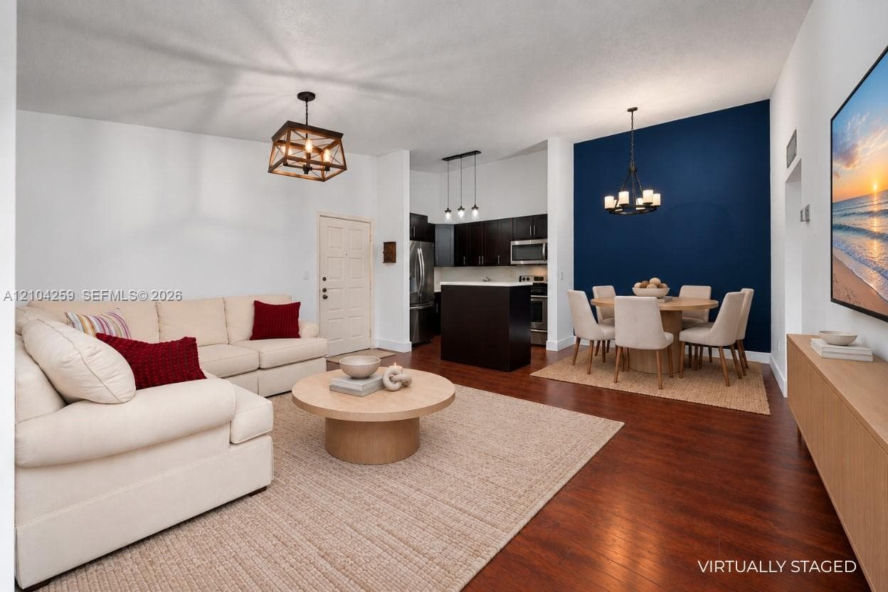 Open-concept area featuring wood-finish flooring, a kitchen island, dark cabinetry, and distinctive decorative pendant and chandelier lighting