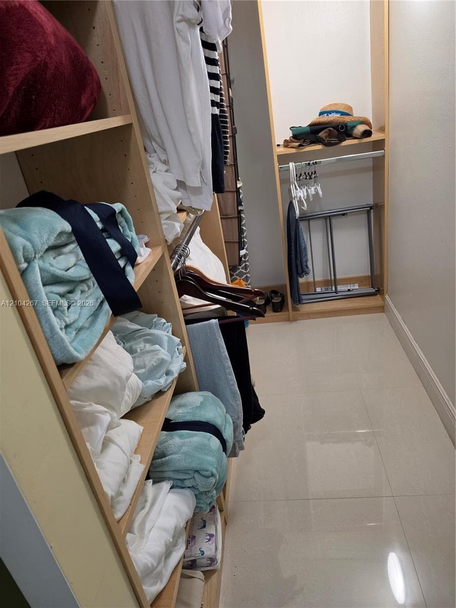 Walk-in closet featuring light-toned custom shelving, integrated storage cubbies, and large-format tile flooring