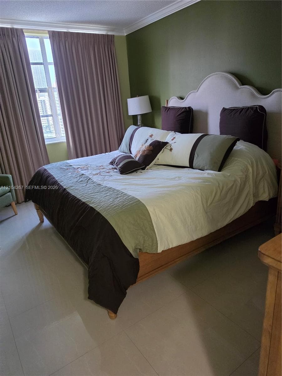 Neutral tile flooring, crown molding, and large-format window with exterior exposure