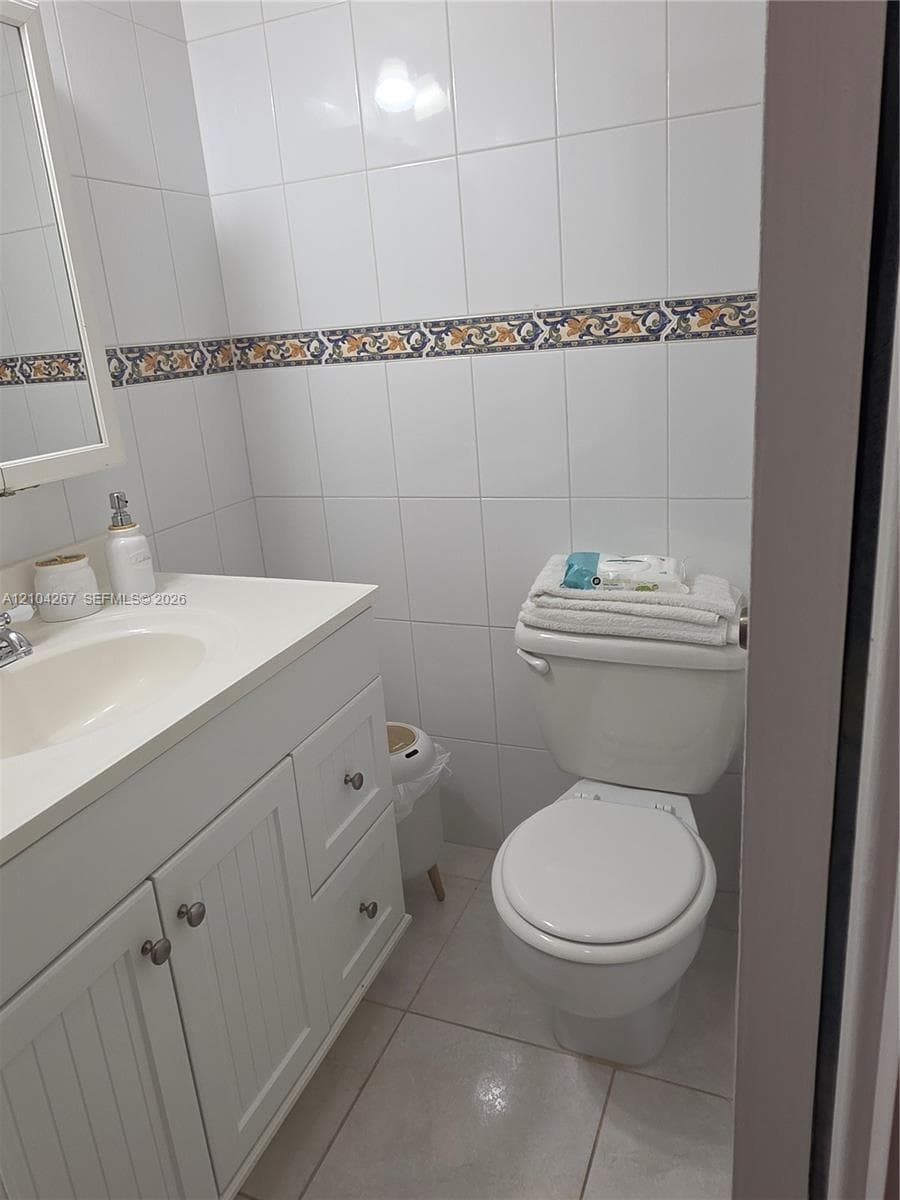 White cabinetry vanity with a solid-surface countertop and integrated sink, complemented by neutral tile flooring and full-height wall tiling featuring a decorative accent border