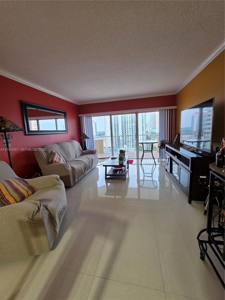 Living area featuring large-format tile flooring, crown molding, and floor-to-ceiling sliding glass doors opening to an outdoor balcony