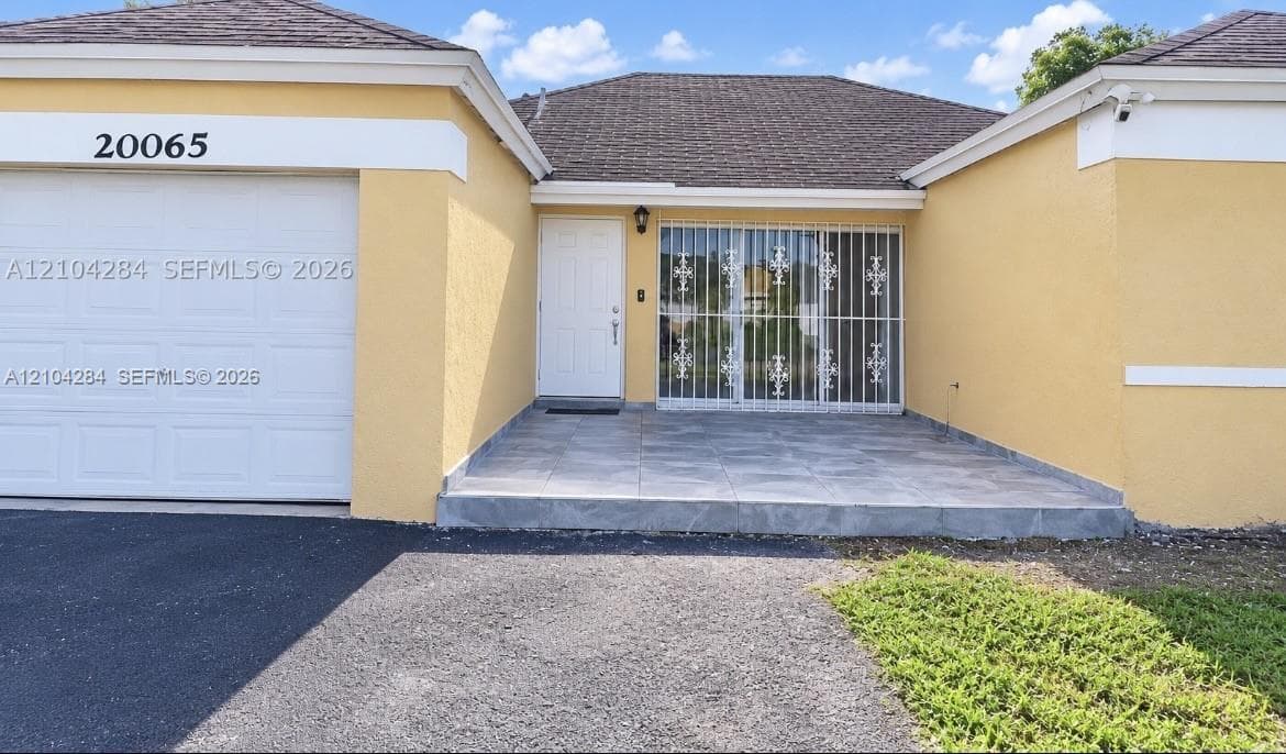 Single-story stucco exterior featuring a hipped roof, attached garage, metal security window bars, and perimeter fencing