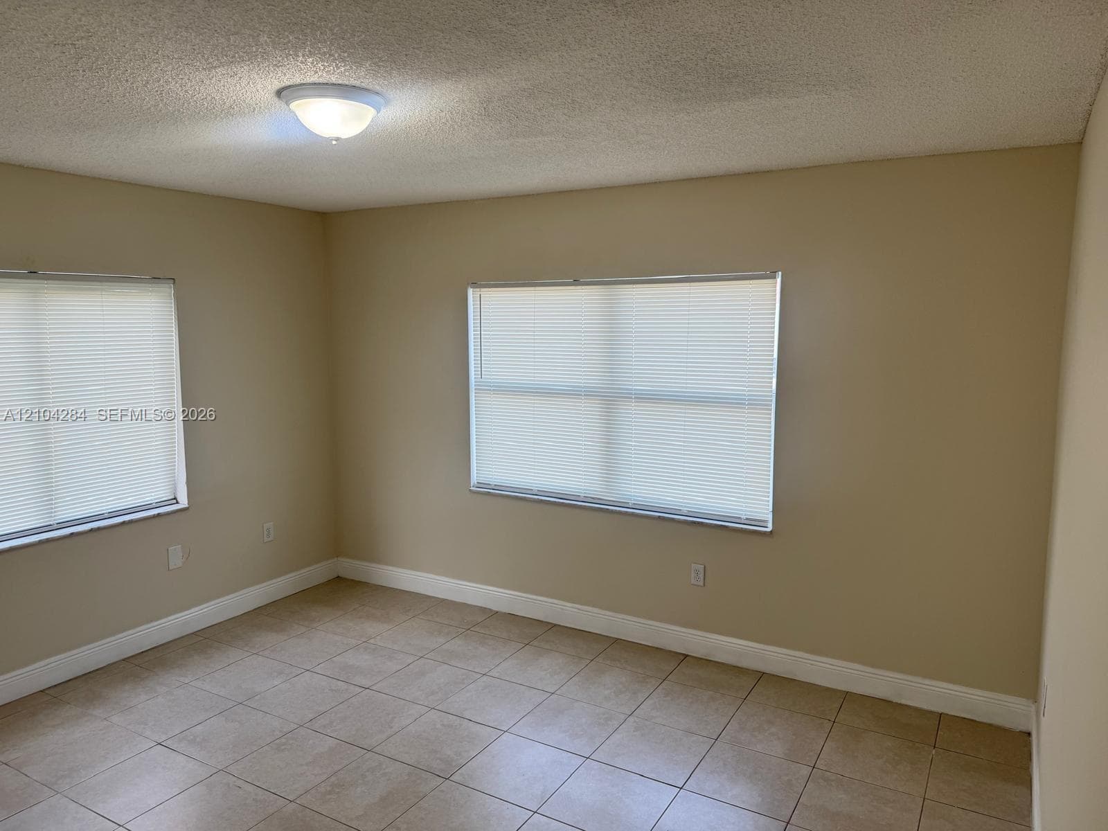 Interior space featuring neutral-toned tile flooring, two double-panel closet doors, and a window with horizontal blinds