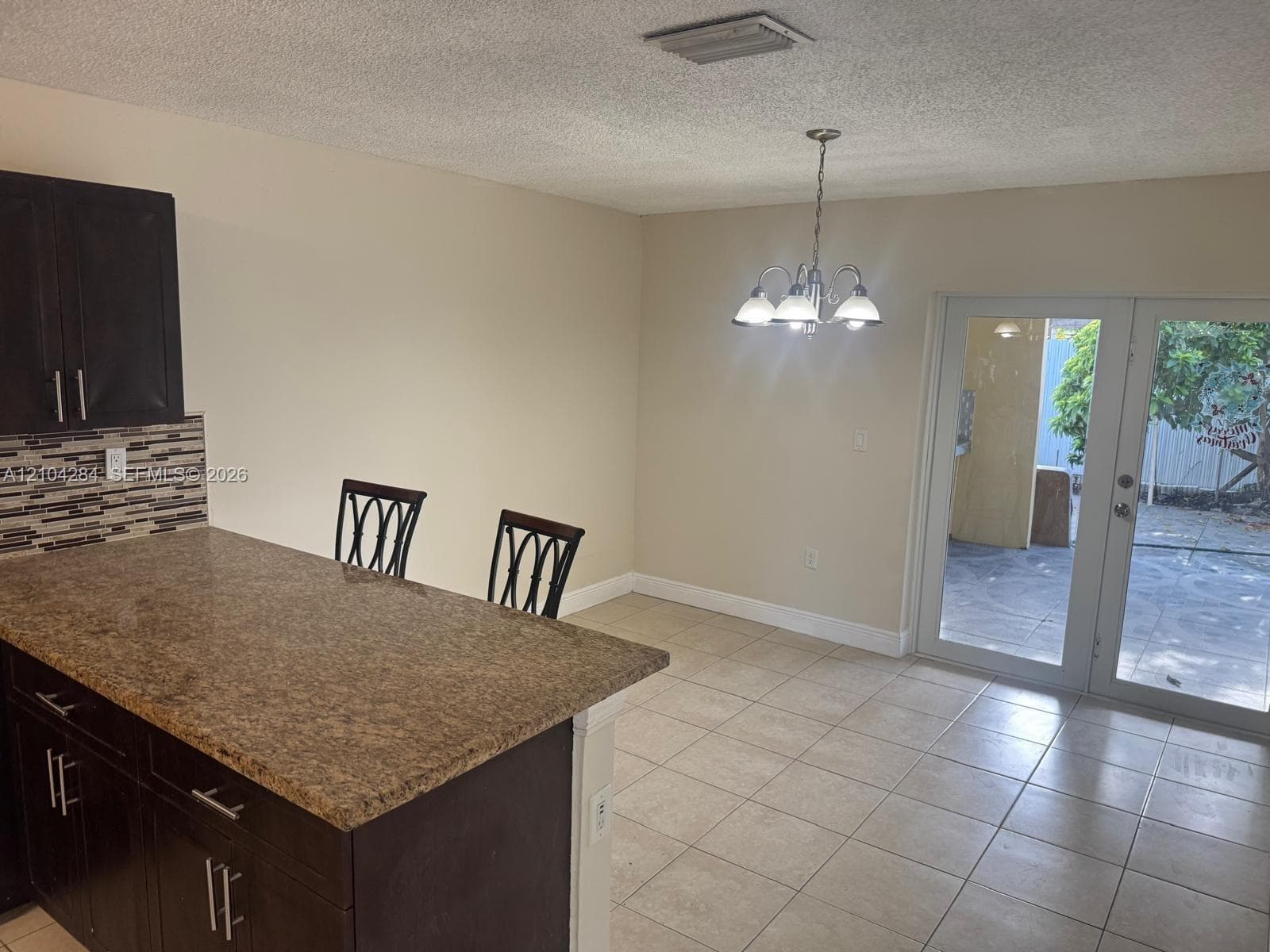 Kitchen featuring dark wood-finish cabinetry, stainless steel appliances, a stone-pattern countertop, tile backsplash, and ceramic floor tiling
