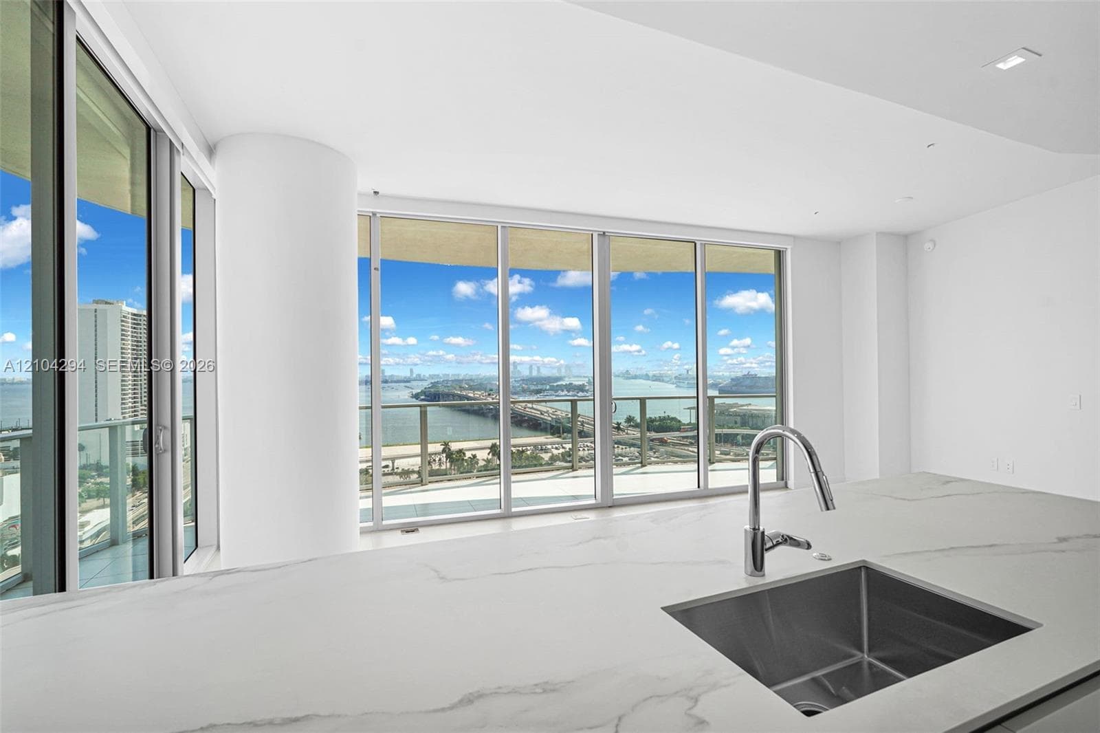 Expansive floor-to-ceiling windows, white countertop with veining, under-mount stainless steel sink, contemporary chrome pull-down faucet, recessed ceiling lighting
