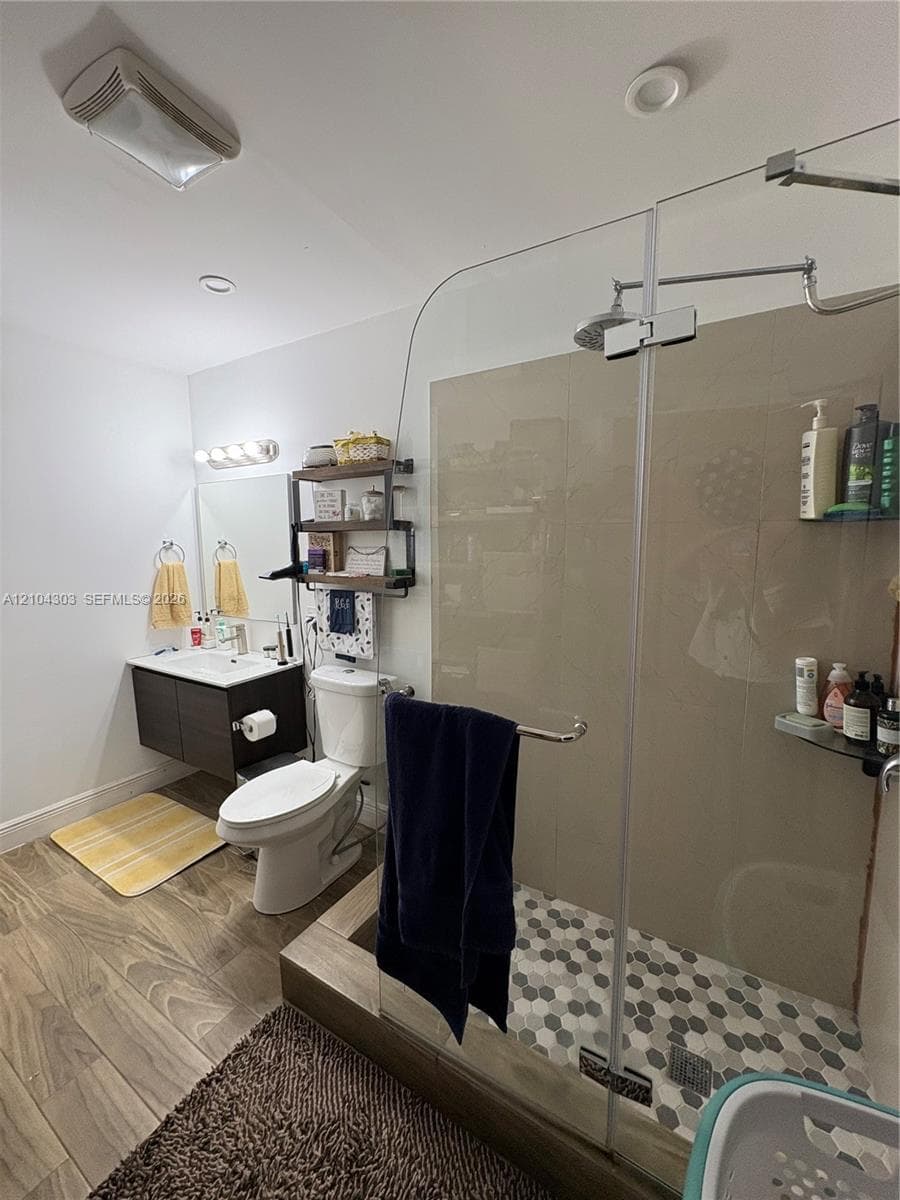 Wall-mounted dark wood-finish vanity with an integrated basin, frameless glass walk-in shower enclosure, oversized stone-finish wall tile, and hexagonal floor tile in the shower