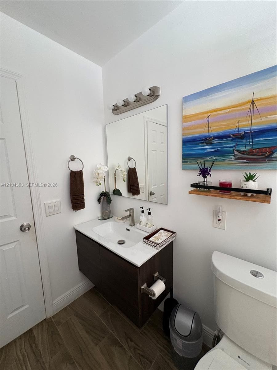 Floating vanity with a white countertop and rectangular basin, integrated mirror, multi-light brushed-nickel fixture, and wood-finish tile flooring