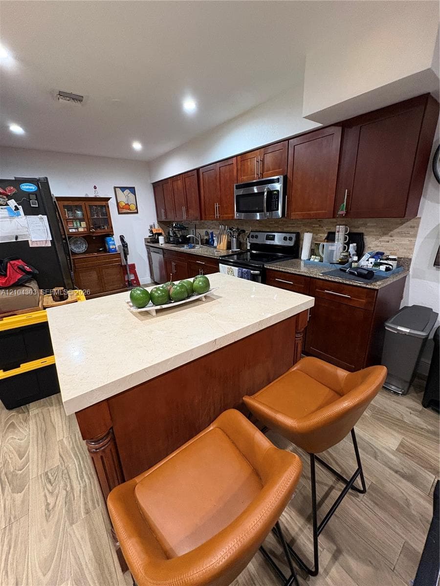 Kitchen featuring dark-toned wooden cabinetry, stone-finish countertops, a central island with a stone surface, and wood-finish flooring