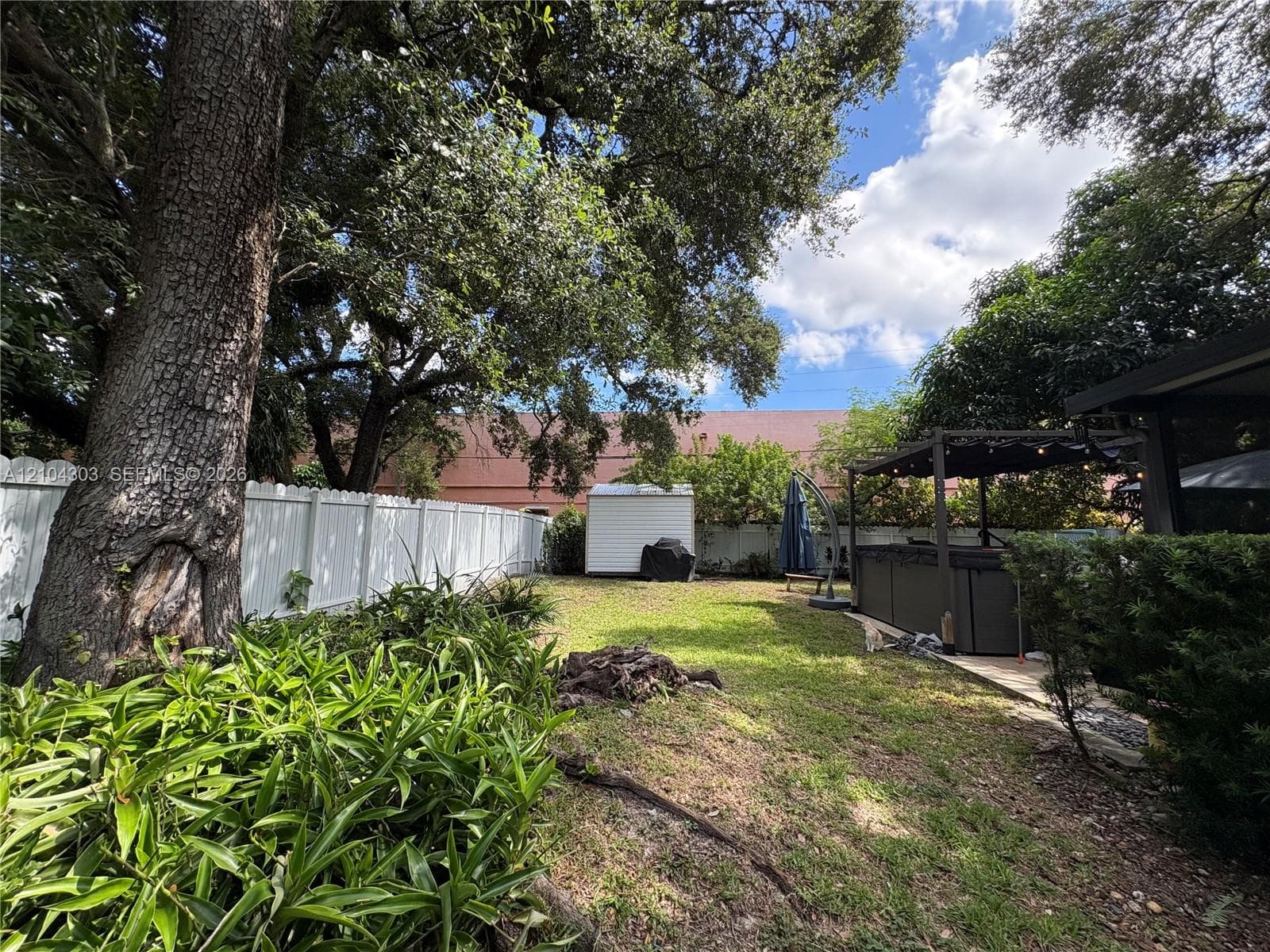 Private backyard featuring a white vinyl privacy fence, mature trees, manicured landscaping, and a covered pergola structure