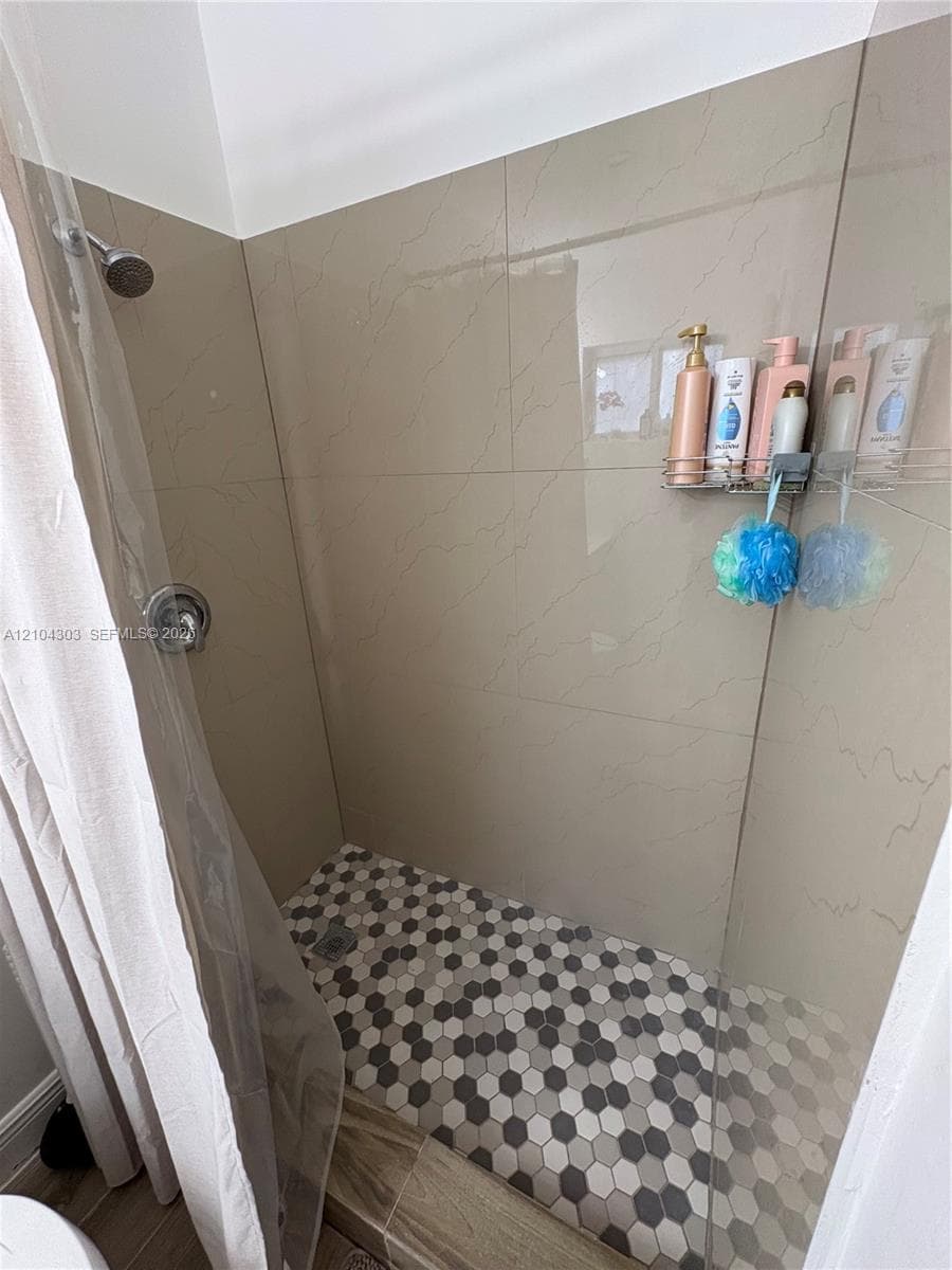 Walk-in shower featuring large-format wall tile, a glass shower panel, and a geometric hexagonal tile floor