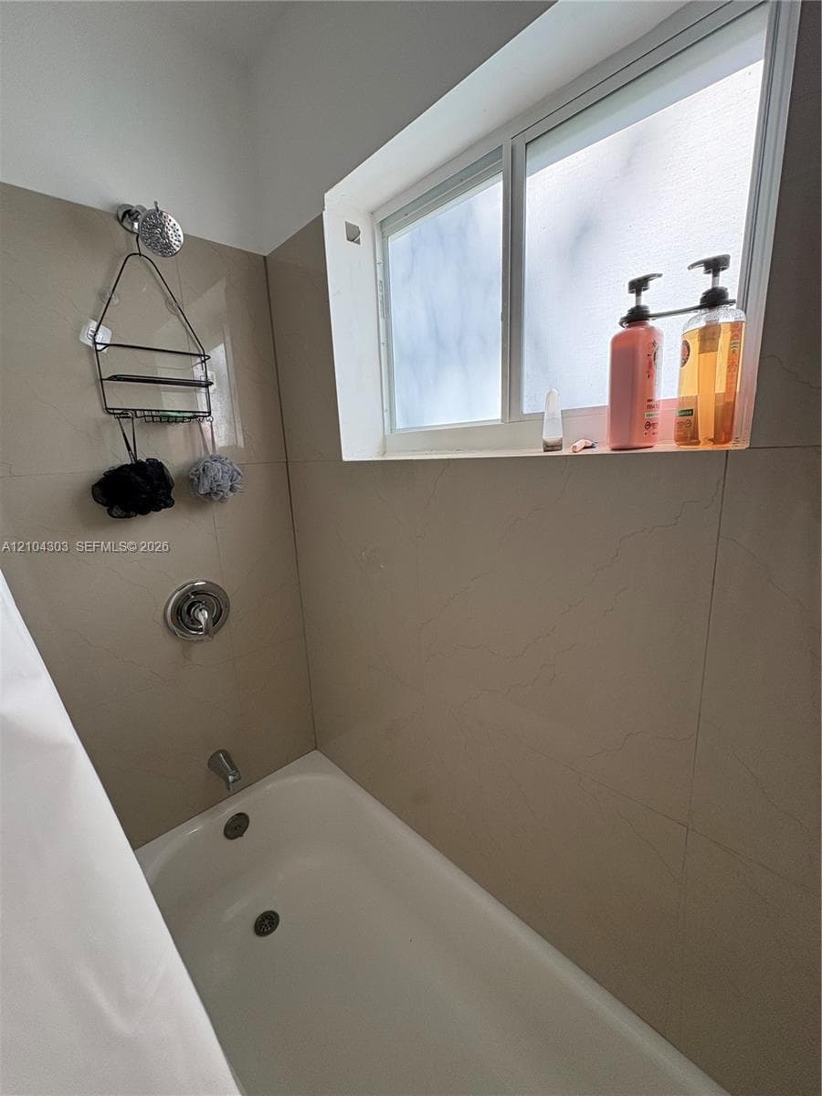 Shower and bathtub combination featuring large-format neutral tile surround, chrome fixture set, and sliding privacy-glass window