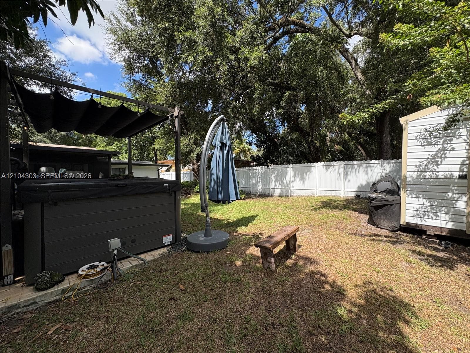 Backyard featuring a privacy-fenced perimeter, a spa with a retractable overhead canopy, and mature shade trees