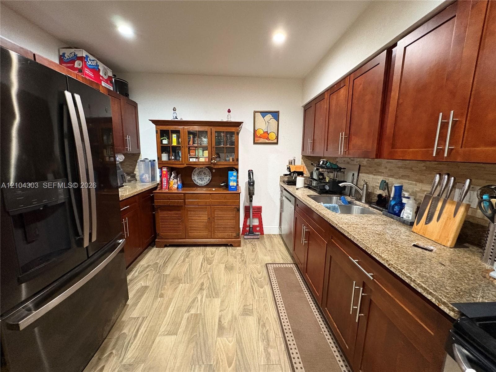 Kitchen featuring warm-tone wood cabinetry, stone countertops, stainless steel sink with a high-arch faucet, tile backsplash, and wood-finish flooring