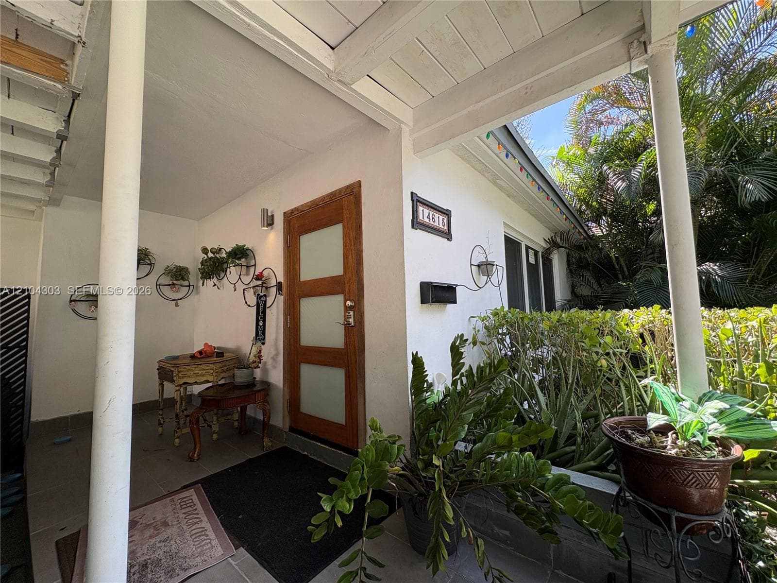 Covered porch featuring a wood-framed front door with frosted glass panels, smooth stucco exterior, and painted structural columns