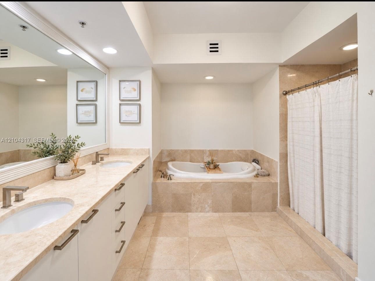 Dual-sink vanity with stone countertop, drop-in soaking tub, stone-tile surround, and full-width wall mirror