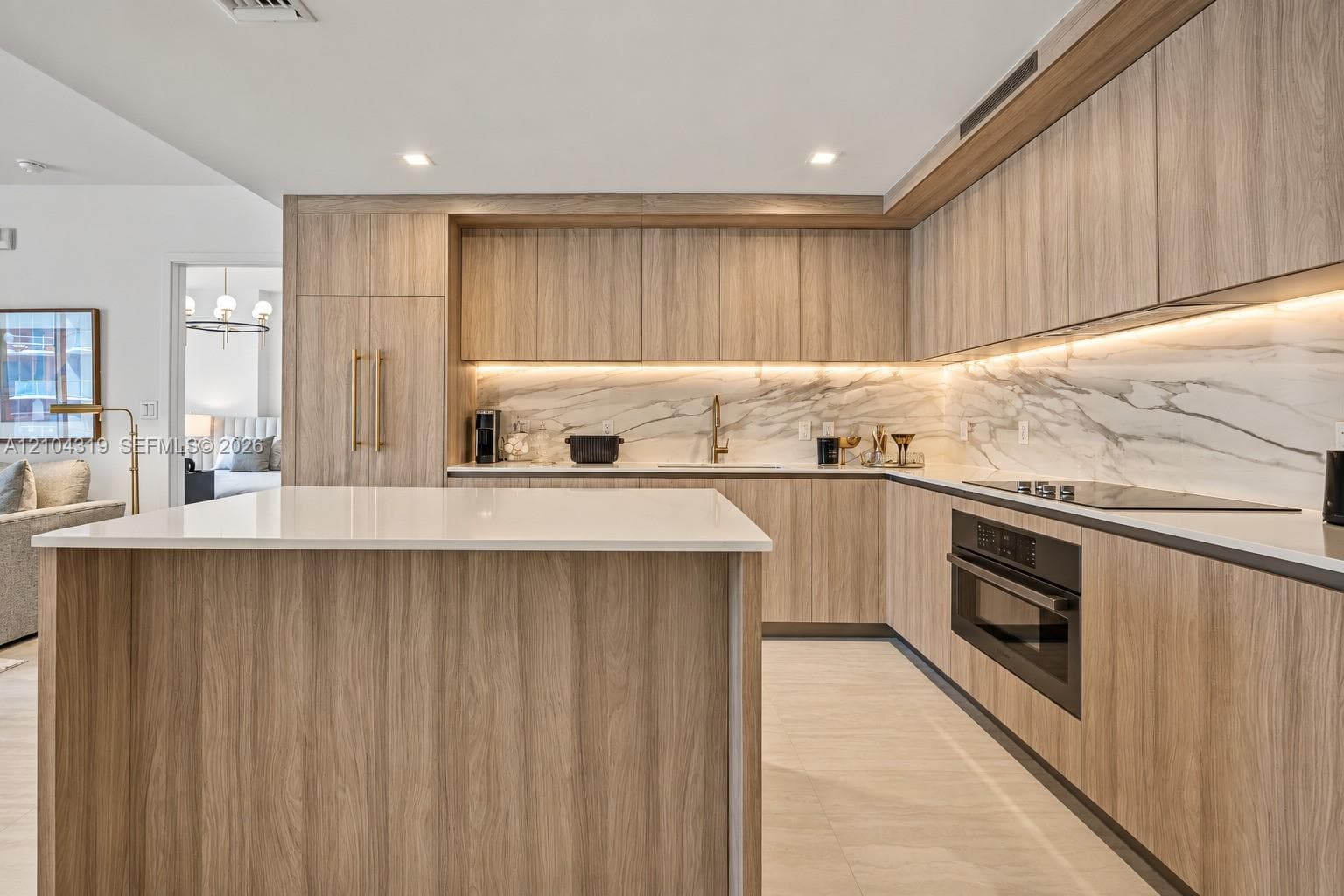Kitchen featuring custom wood-finish cabinetry, a white stone island countertop, integrated appliances, and a full-height stone backsplash with under-cabinet lighting