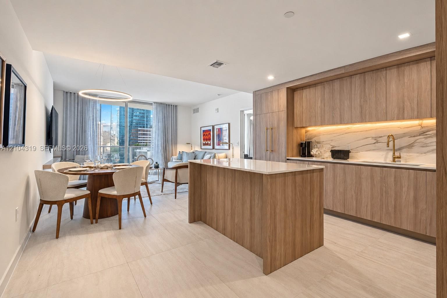 Modern kitchen featuring wood-finish cabinetry, a central island with a stone-surface countertop, integrated appliances, under-cabinet lighting, and stone-tile flooring