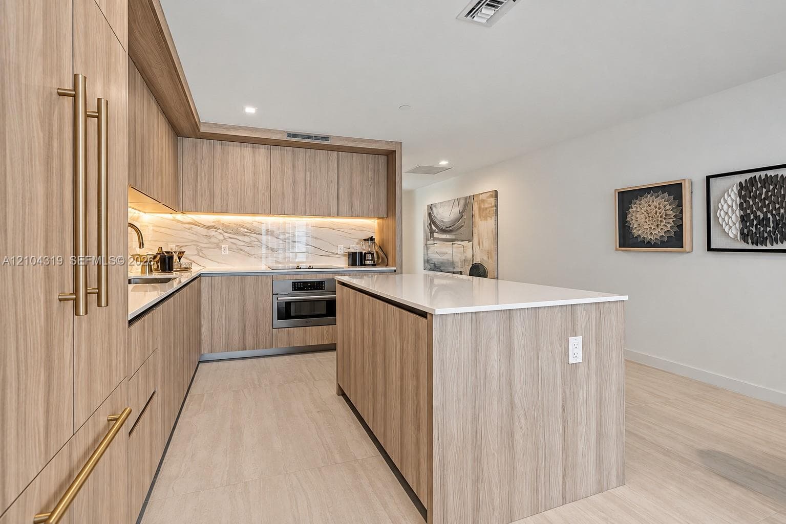 Kitchen featuring wood-finish cabinetry, a large central island with a quartz countertop, integrated under-cabinet lighting, and a stone-style backsplash