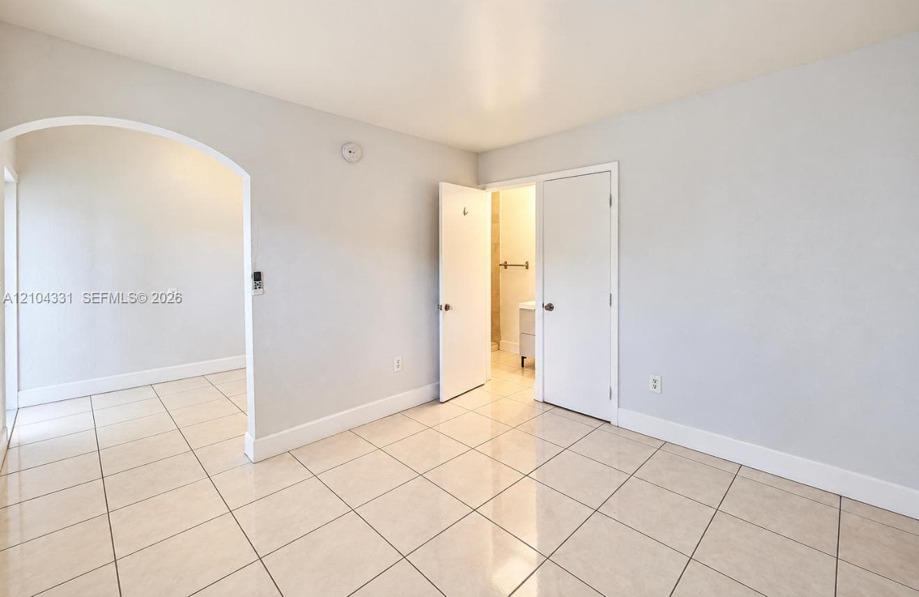 Interior space featuring neutral wall tones, large-format tile flooring, a prominent arched doorway, and solid-core interior doors